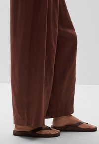 Brown wide-leg trousers made of lightweight fabric, paired with brown flip-flops featuring cross straps and a flat sole.