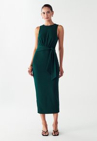 Tamnozelena haljina bez rukava s pripijenim krojem, detaljem za vezivanje u struku i duljinom do sredine lista. Glatka tekstura i jednostavan dizajn.