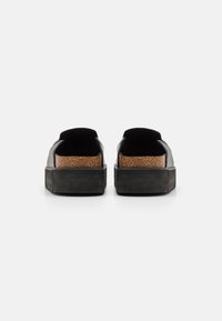 Svarta slip-on-skor med övre i texturerad läder och korkinlägg. Har en tjock gummisula och en minimalistisk design.