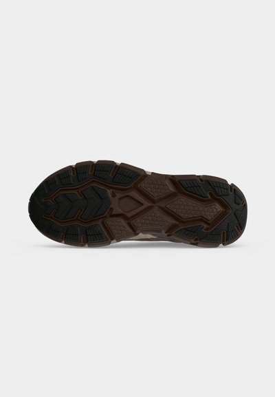 Semelle de chaussure avec un motif robuste combinant caoutchouc noir et brun pour l'adhérence et la durabilité sur un fond clair uni.