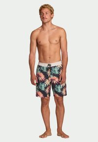 Muške kupaćice s tamnom pozadinom, ukrašene živopisnim tropskim cvjetnim uzorcima u zelenoj, ružičastoj i žutoj boji. Elastična traka u struku s vezicom.