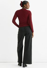 Red textured long-sleeve top paired with high-waisted wide-leg black jeans. Model wears black heeled shoes and a matching scrunchie.