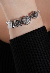 Zilveren bedelarmband met een handtas, kinderwagen, klaver, hart en textuurelementen. De bedels zijn versierd met kristallen en ingewikkelde details.