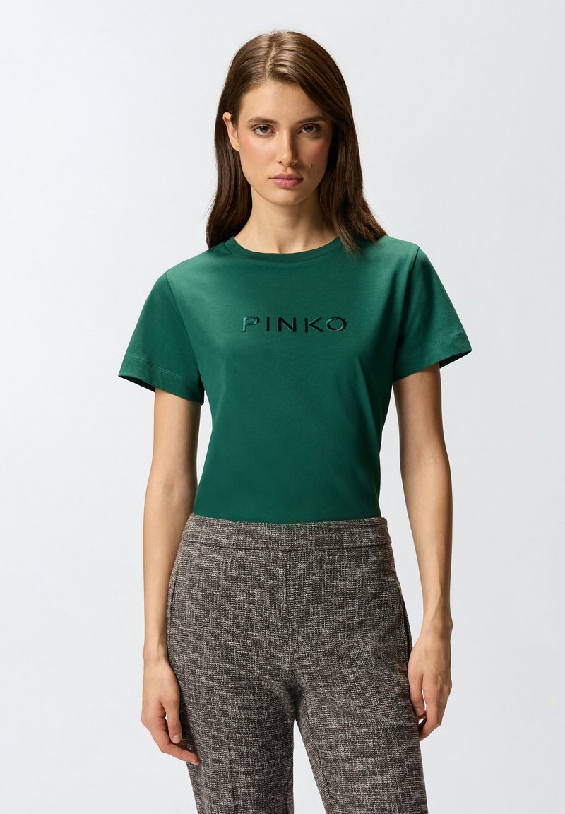 Zeleni pamučni majica kratkih rukava s reljefnim logotipom "PINKO" na prsima, u kombinaciji s teksturiranim smeškim hlačama.