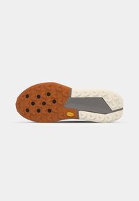 Semelle en caoutchouc mélangeant orange et crème, dotée de crampons multidirectionnels pour une meilleure adhérence, et d'un panneau central gris avec un logo.