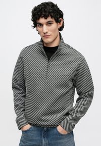 Pulover gri și negru cu un fermoar scurt în partea superioară, cu model houndstooth, mâneci lungi și suprafață texturată, asortat cu blugi din denim.