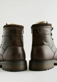Botas de cuero marrón con un acento de ante texturizado, forro de piel de fur en la parte superior y una suela de goma resistente con un diseño de madera estratificada.
