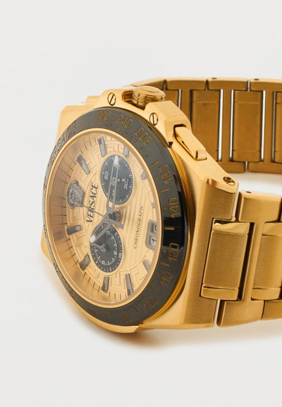 Auksinis Versace chronografo laikrodis su juodu bezeliu, tachimetro žymėmis, dviem subciferblatais, datos langeliu ir metalinės grandinėlės apyranke.