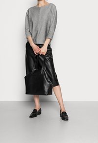 Harmaa neulottu paita, jossa on 3/4-hihat, musta keinonahkainen-midi-hame ja musta käsilaukku, yhdistettynä mustiin mokkasiineihin, seisoo vaalealla pinnalla.