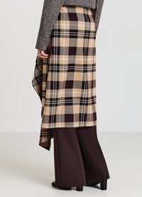 Gonna a quadri in beige, marrone e grigio con orlo asimmetrico. Abbinata a pantaloni ampi color marrone scuro e stivali con tacco neri.