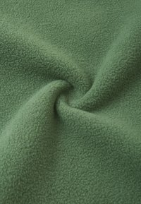 Zielony polar o miękkiej, teksturowanej powierzchni, z lekko strzępiącym się wyglądem i gładkim, skręconym brzegiem.