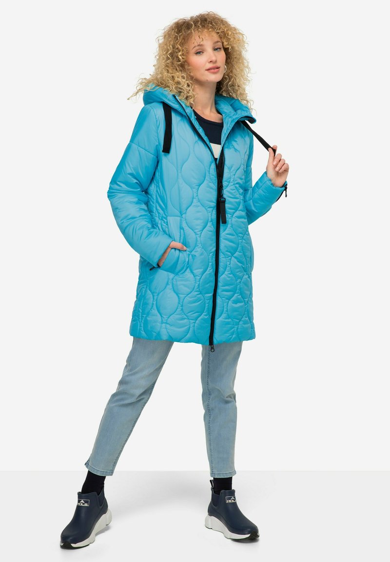 Light blue quilted puffer jacket with a hood, black accents, zippered pockets, and a relaxed fit, paired with light jeans and dark boots.