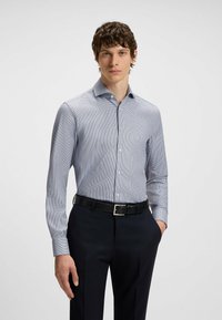 Camicia da uomo button-down a scacchi blu e bianchi, con maniche lunghe, colletto e una texture di tessuto liscia, abbinata a pantaloni scuri.