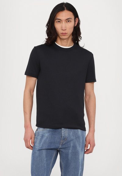 Svart bomulls t-skjorte med korte ermer, rund hals, og kontrasterende hvit innerkrave. Brukt sammen med lyseblå denimjeans.