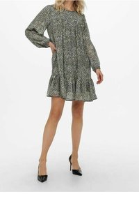 Vestido verde con estampado de leopardo, de manga larga, con dobladillo rizado y fabricado en tejido ligero; combinado con zapatos de tacón negros.