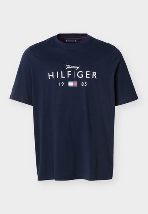 Navyblaues T-Shirt mit kurzen Ärmeln, auf dem vorne der Schriftzug "Tommy Hilfiger 1985" sowie ein kleines Logo in Form einer roten, weißen und blauen Flagge zu sehen sind.