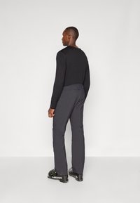 Černá dlouhá rukávová košile spárovaná s tmavě šedými kalhotami. Kalhoty mají elegantní střih a jemnou texturu. Černé boty doplňují celkový vzhled.