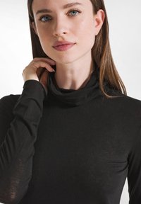 Schwarzes Rollkragenoberteil aus leichtem Stoff, mit langen Ärmeln und einem weichen, leicht taillierten Design, das einen engen Ausschnitt und eine minimale Textur aufweist.