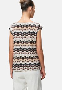 Multicolored zigzag patterned top in beige, black, and rust tones. Textured knit fabric with short sleeves and a rounded neckline.