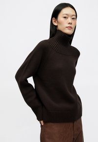 Maglione marrone chunky in maglia, con colletto alto a coste, vestibilità rilassata e spalle scese, caratterizzato da un tessuto testurizzato e polsini a coste.