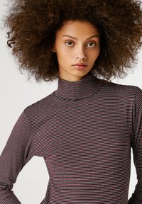 Noor noor, kellel on mahukad lokkis juuksed, kannab sobivat triibulist kõrge kaelusega kampsunit mustade, valgete ja burgundia toonidega.