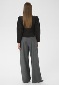 Bluză neagră scurtă cu mâneci bufante, asociată cu pantaloni largi din carouri gri, având un model discret în carouri și o siluetă elegantă.