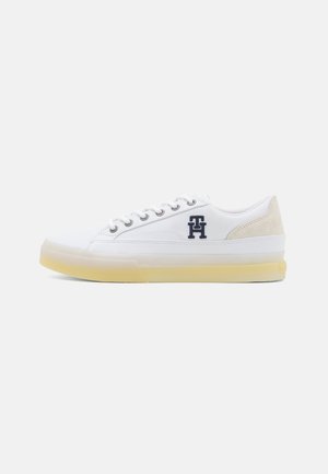 Sneaker bianco in tela con accenti in suede beige, punta rotonda, sei occhielli metallici e suola in gomma traslucida gialla. Presenta il logo sul lato.