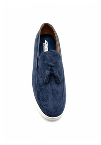 Chaussure slip-on en suede marine avec des glands décoratifs, texture lisse, semelle en caoutchouc et semelle extérieure blanche contrastante, avec un intérieur de couleur marron.