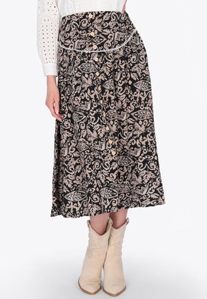 Donna che indossa una gonna midi nera con motivi floreali beige, dettaglio con bottoni sul davanti, camicetta bianca con trafori e stivaletti beige.