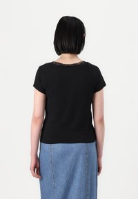 Svart t-skjorte med korte ermer og blonder rundt halslinjen, sammen med et lys blått denimskjørt. Baksiden viser en figursydd silhuett.