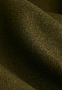 Tela de lana en verde oliva con una superficie suave y texturizada, que presenta pliegues suaves y sutiles variaciones en la tonalidad.