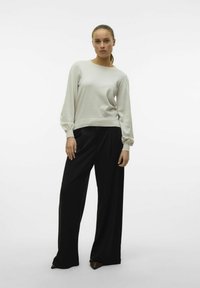 Pull long gris clair avec texture côtelée, associé à un pantalon large noir ample. La tenue présente une coupe décontractée et un design simple.
