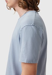 T-shirt azzurro chiaro a maniche corte con una vestibilità morbida, una texture sottile e bordi grezzi sul collo e sulle maniche.
