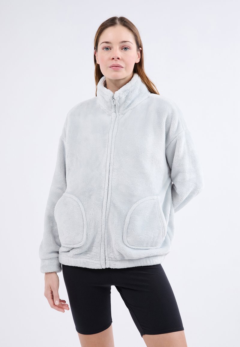 Veste en polaire synthétique gris clair, avec un col haut, une fermeture éclair à l'avant et de grandes poches arrondies. Texture douce, coupe décontractée et épaules tombantes.