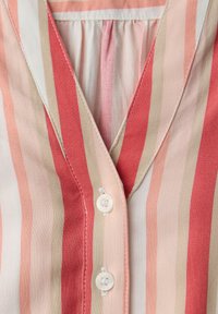 Gros plan d'un vêtement à rayures verticales rouges, roses, beige et blanches, avec un col en V et deux boutons blancs à l'avant.