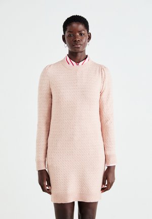 Rosa strukturiertes Strickkleid mit langen Ärmeln und einem gerippten Saum. Darunter ist ein kragenloses rot-weißt gestreiftes Hemd sichtbar.
