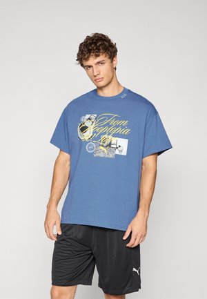 Blå grafisk t-shirt med korte ærmer, der har gule trykte tekster og forskellige grafiske former; parret med sorte shorts.