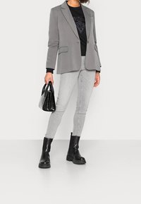 Blazer gris sobre un suéter negro, combinado con jeans ajustados gris claro y botines gruesos negros. Lleva un pequeño bolso negro con estampado de cocodrilo.