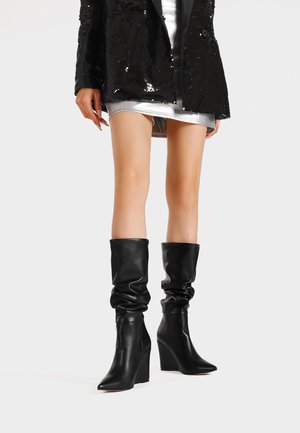 Stivali neri in pelle fino al ginocchio con un design morbido, punta a forma appuntita e tacco a zeppa. Texture liscia, stile minimalista, senza motivi visibili.