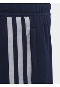 Navyblauwe trainingsbroek met witte verticale strepen, gestructureerde stof, elastische band en zijzak met ritsdetail.