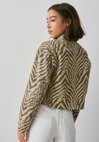 Hnedo-bežová skrátená bunda so zmesou zebrových a leopardích vzorov, s voľným strihom a dlhými rukávmi.