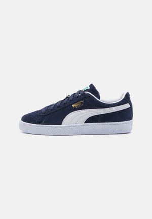 Marineblaue Puma Wildleder-Sneaker mit weißem Streifen, weißer Sohle, Schnürsenkeln und goldenem Puma Suede-Logo an der Seite.