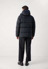 Zwarte pufferjack met een capuchon, met een gequilt ontwerp en gestructureerde stof. Draag het met zwarte broek en schoenen in een minimalistische setting.