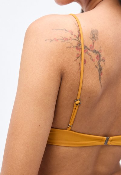 Haut de bikini jaune avec bretelles fines, réglables, et texture lisse ; comporte un tatouage floral sur l'épaule.