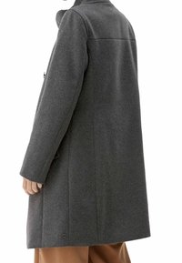 Grå uldfrakke med lige snit, udstyret med høj krave, lange ærmer og en enkelt knapdetalje ved kanten. Minimalistisk design.