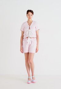 Rosa rutete to-delte antrekk med en cropped topp som har knyting foran og matchende shorts. Modellen har på seg plattform sko i pastellblå og rosa.