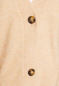 Light beige cardigan featuring a v-neck design, ribbed texture, and three large dark buttons for fastening. Soft, knitted fabric.