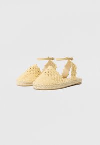 Sandales espadrilles tressées jaunes avec bride à la cheville, présentant un design ouvert, une surface texturée et une semelle en jute tressé.