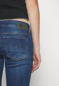 Los jeans ajustados de mezclilla índigo oscuro cuentan con una etiqueta de cuero negro en la parte trasera de la cintura y costuras sutiles en los bolsillos.
