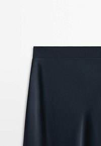 Jupe noire avec une ceinture élastique côtelée et un tissu lisse, montrée de la taille jusqu'au milieu des hanches sur fond blanc.